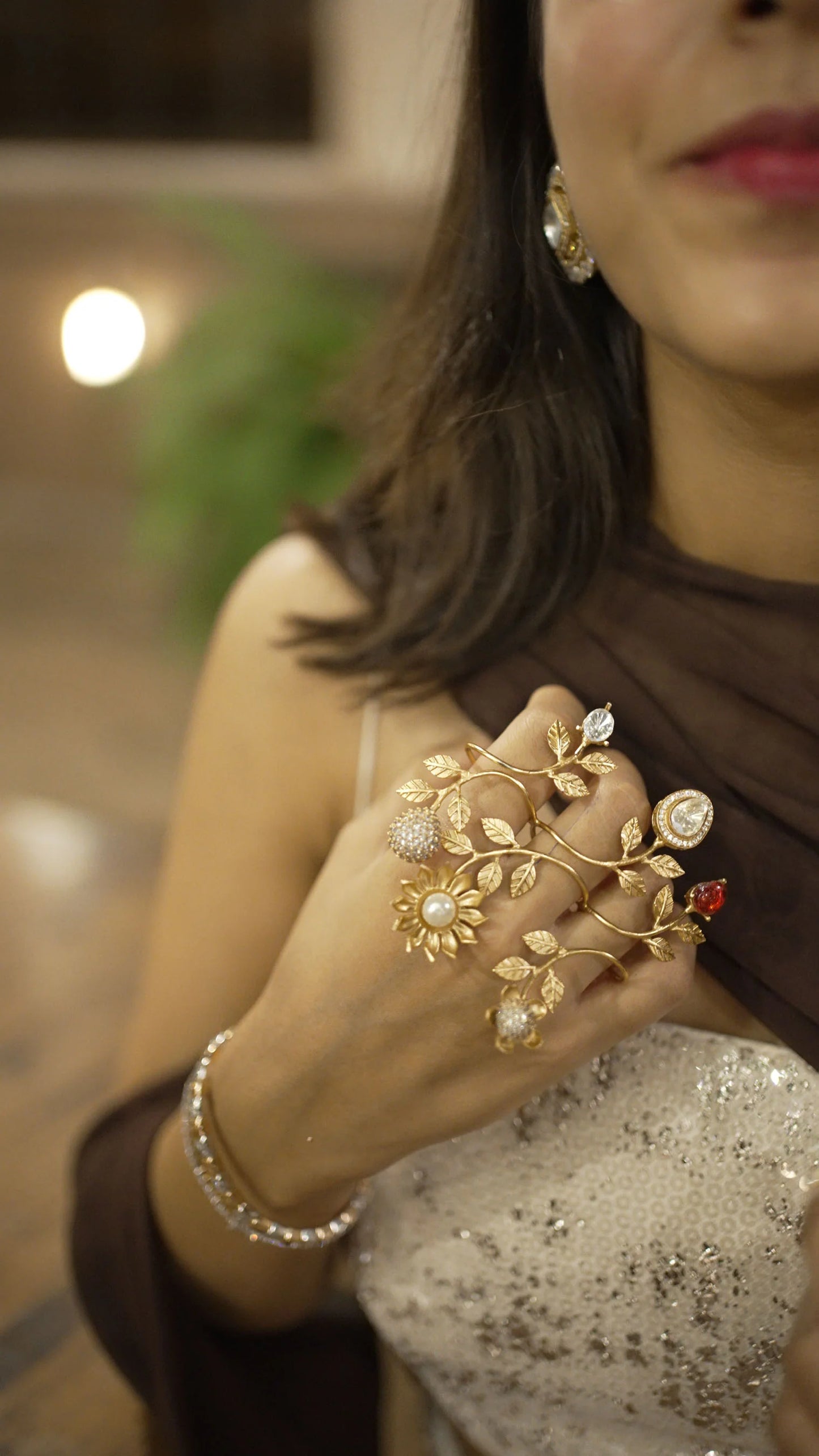 Luxury gold hand jewelry with leaf and flower design worn with statement rings on model
