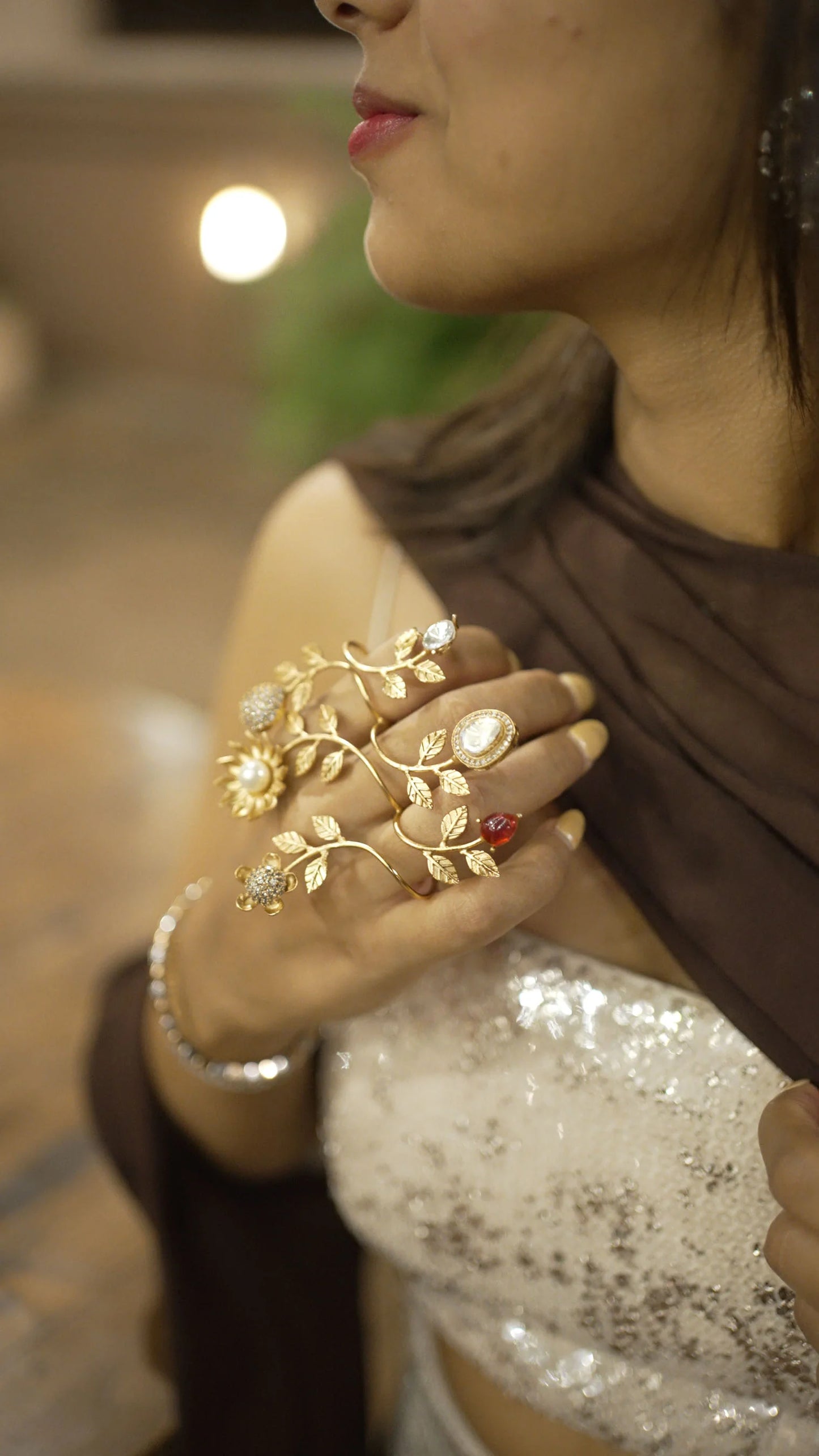 Stylish close-up of gold hand accessory with red and clear gemstones on woman’s hand
