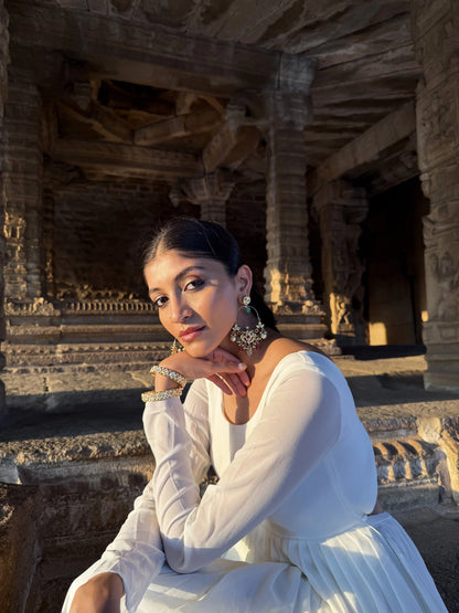 Sophisticated image of a woman in a minimal white outfit highlighting ornate jewelry in a historic temple backdrop
