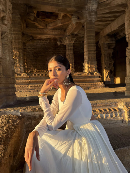Golden hour portrait of a woman seated on stone steps, showcasing intricate earrings and bracelet in a heritage setting
