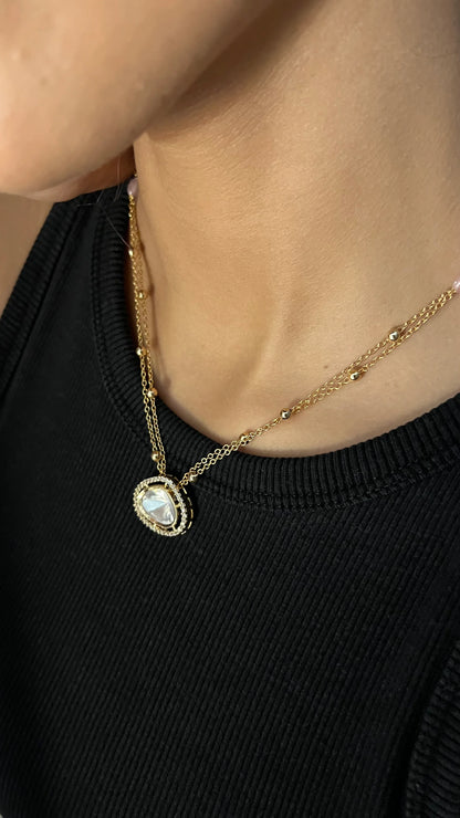 Minimal jewelry close-up highlighting a double-layer chain with subtle gold beads and a luminous teardrop charm.

