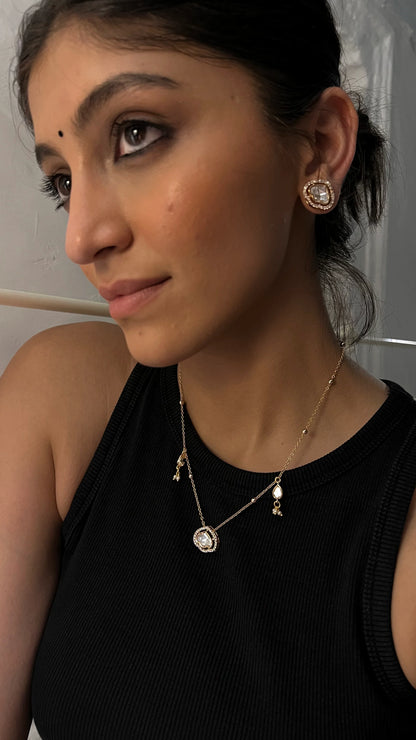 Sophisticated styling image featuring a gold chain duo with a framed pendant centerpiece and understated detailing.
