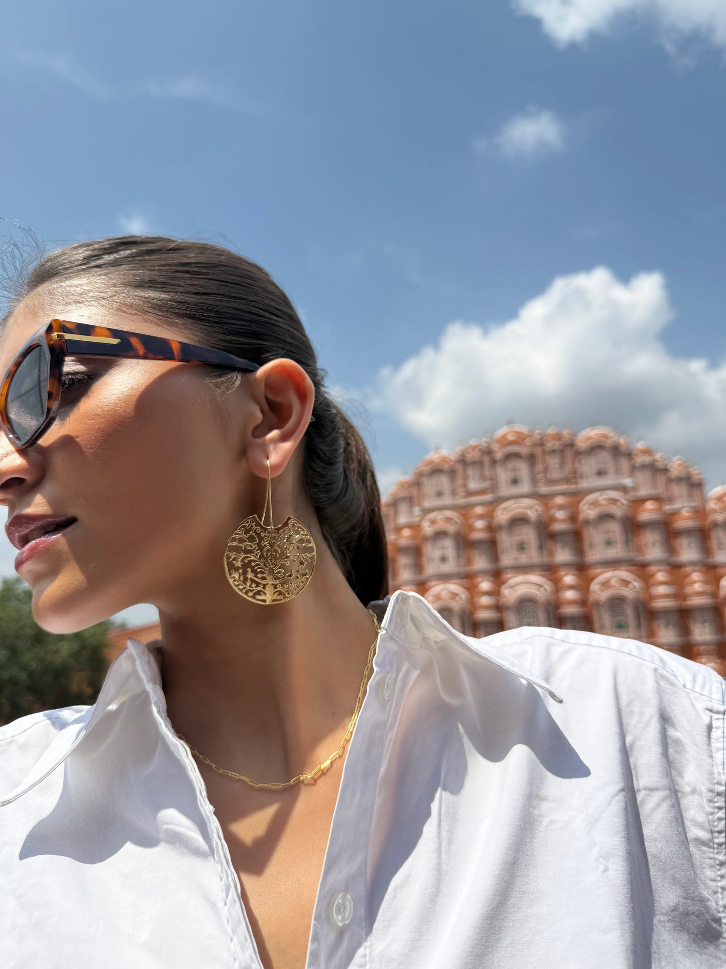 Fashion portrait of woman wearing gold earrings and sunglasses with famous palace in background
