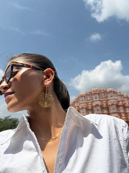 Woman with sleek ponytail wearing gold statement earrings against iconic building backdrop
