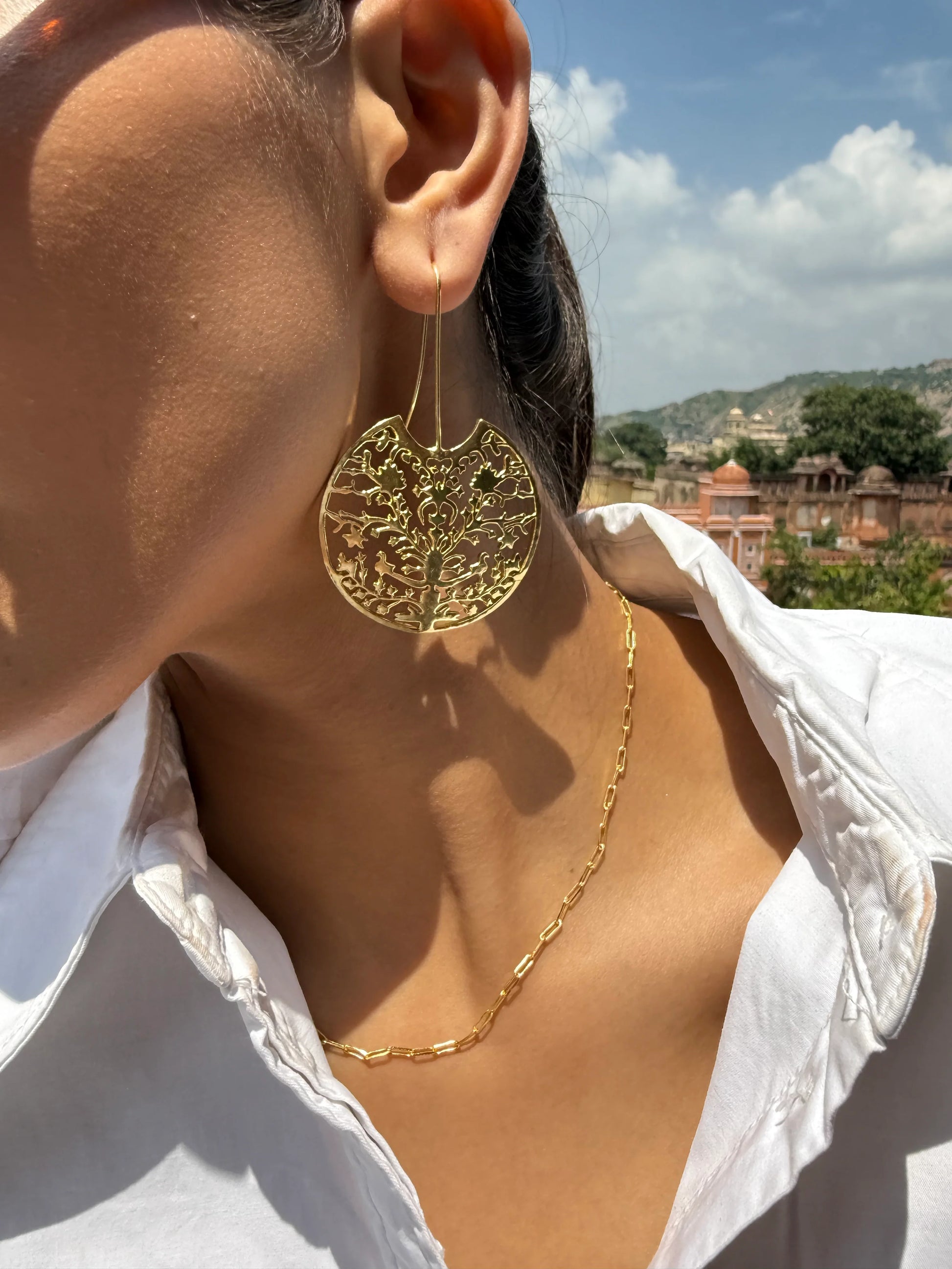 Woman wearing gold jewelry and sunglasses with detailed palace architecture in background
