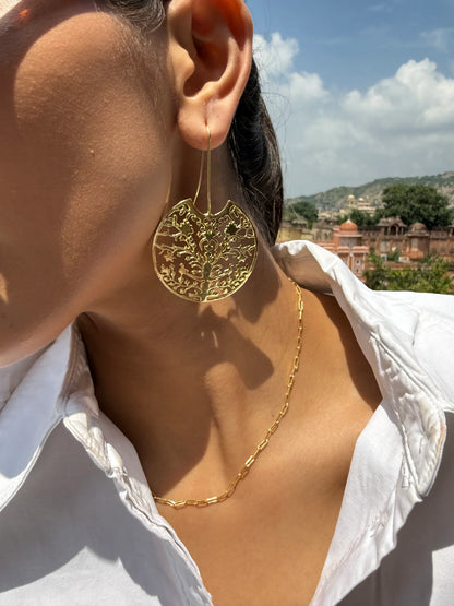 Woman wearing gold jewelry and sunglasses with detailed palace architecture in background
