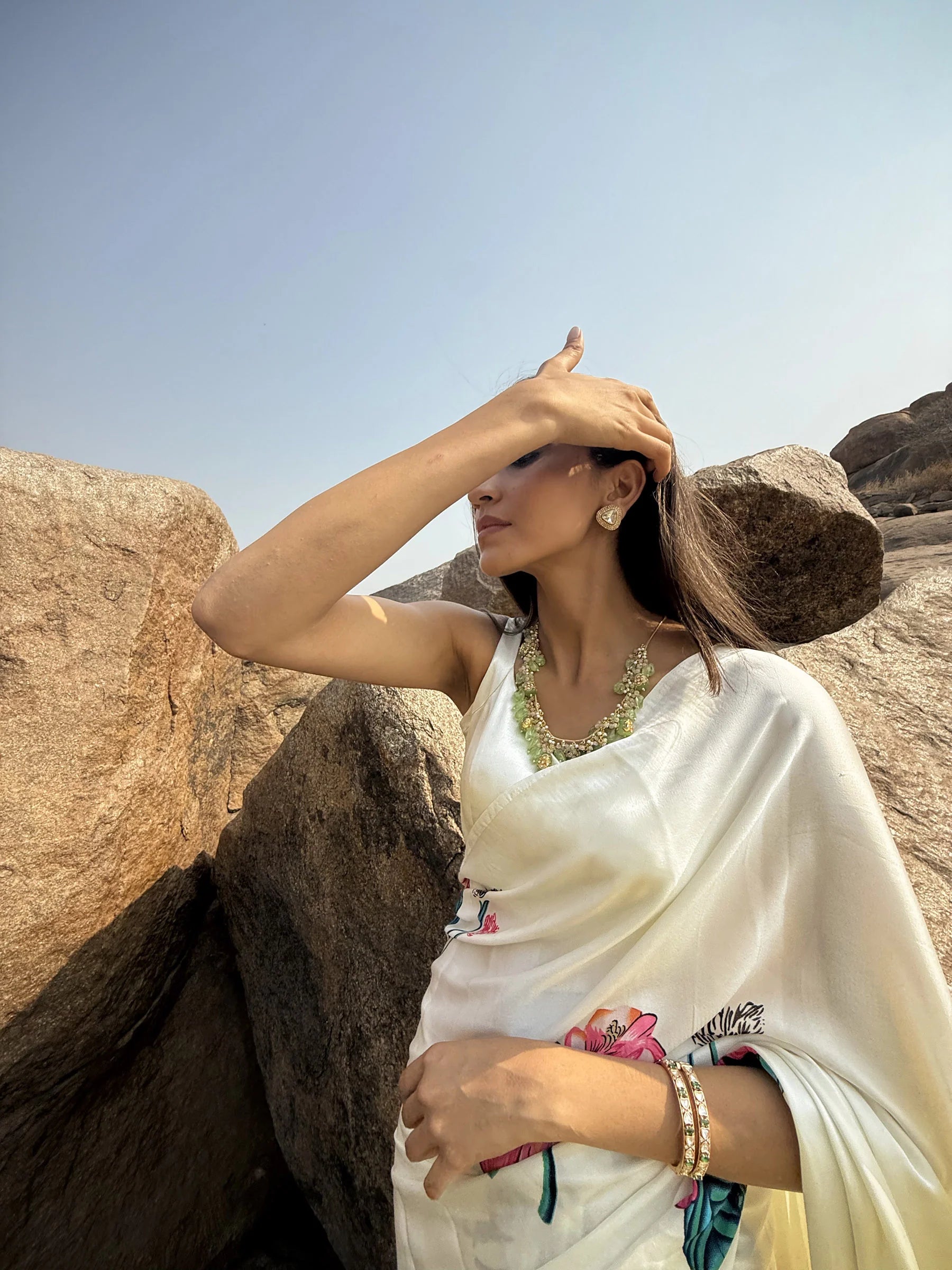 Sophisticated portrait of a woman resting her face on her hand, showcasing intricate rings and a bracelet in a heritage setting.
