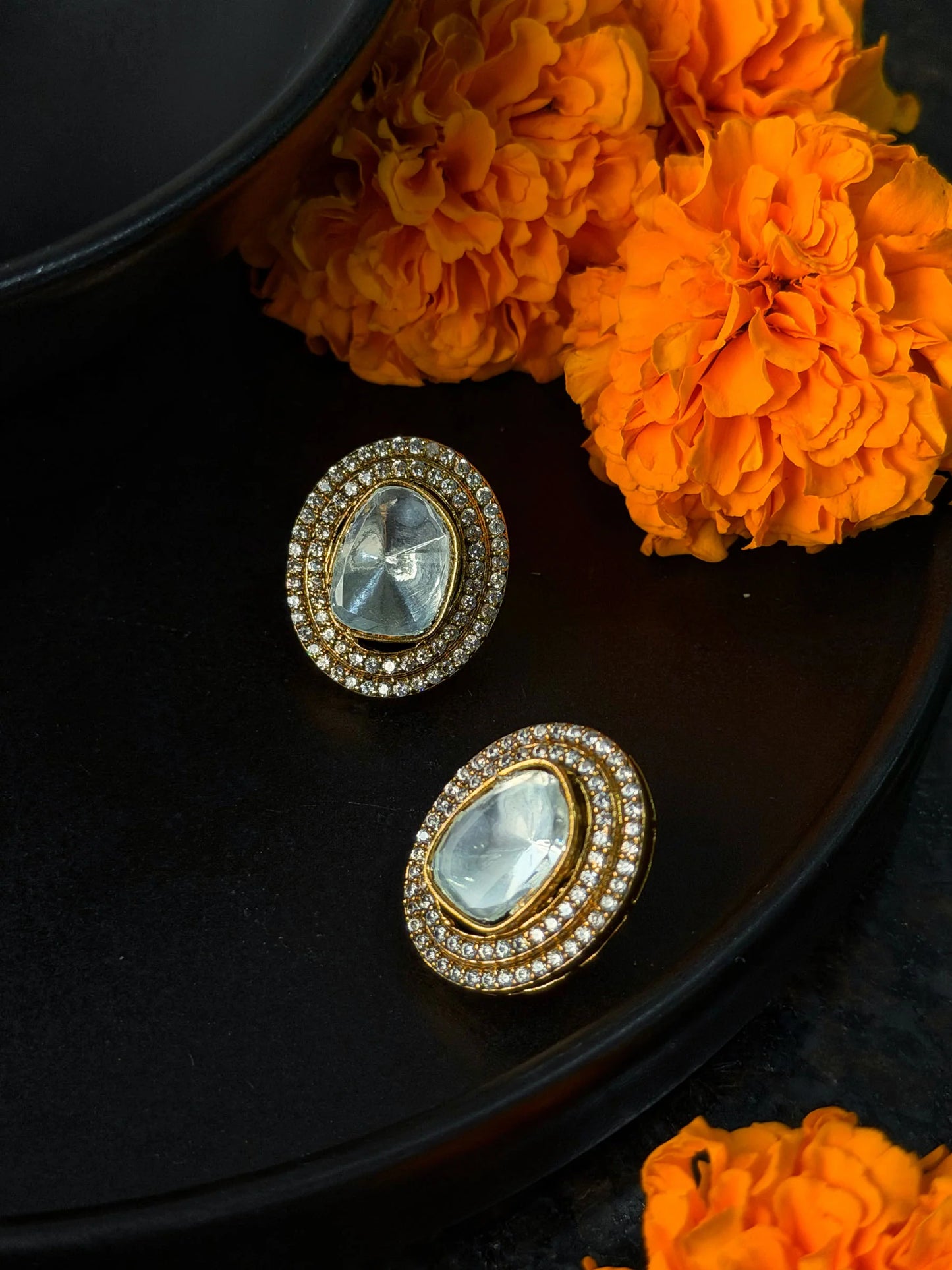 Premium gold oval stud earrings with crystal stones and halo setting in festive styling with marigold backdrop
