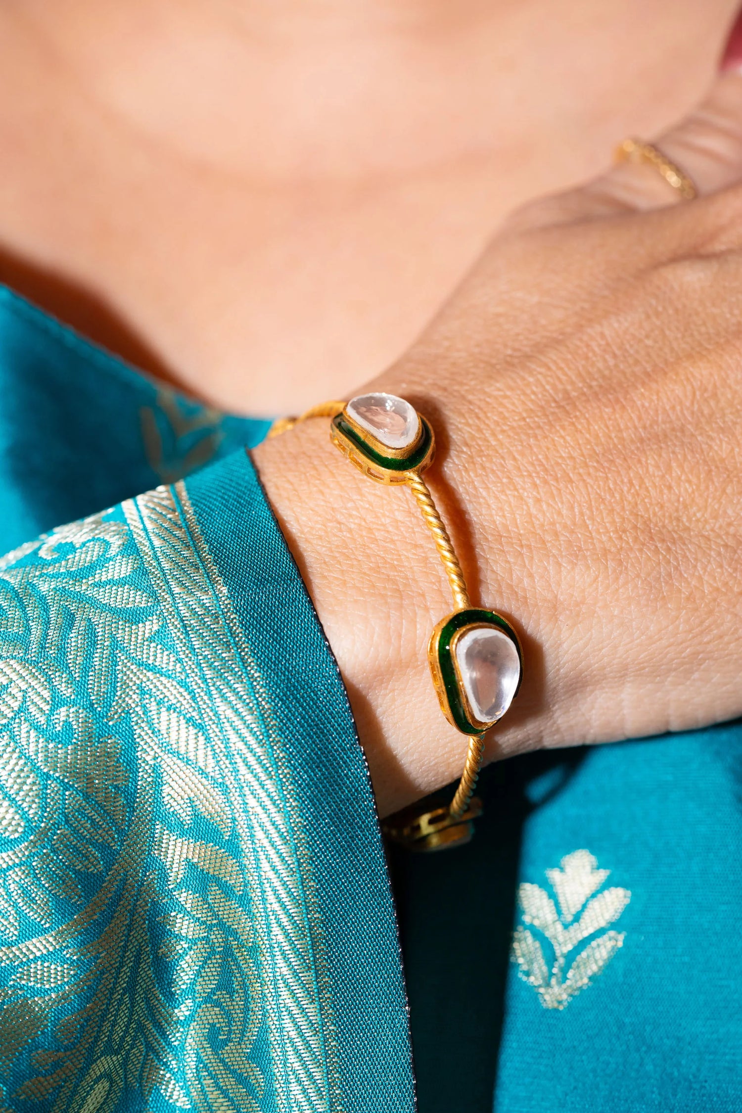 Elegant gold bracelet with clear stones and green detailing worn on hand in traditional attire
