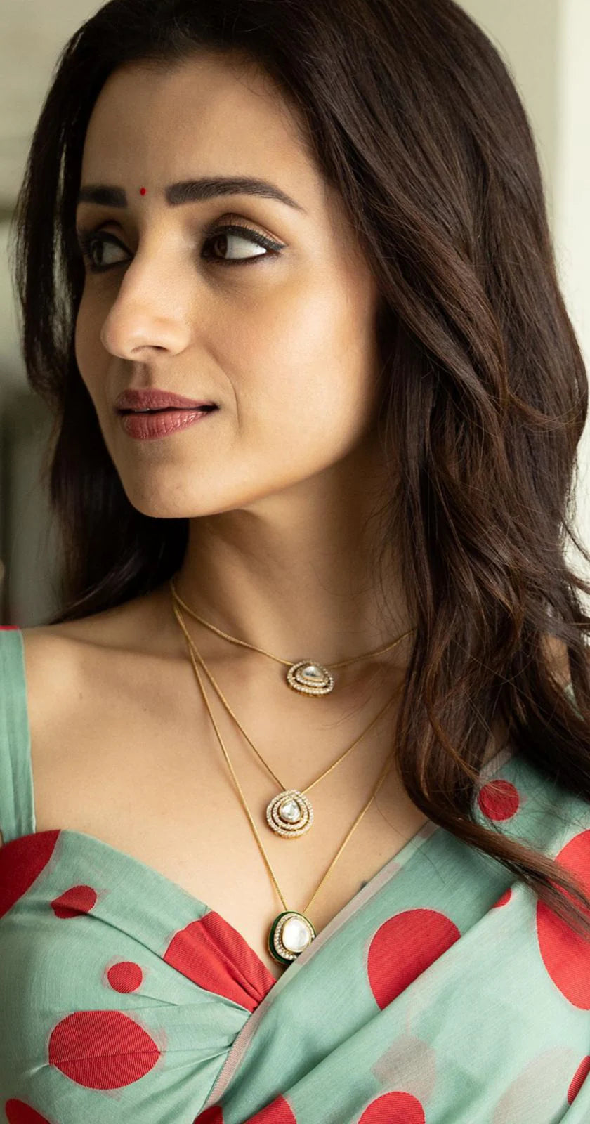 Elegant portrait of a woman in a polka dot saree with delicate gold jewelry in a modern indoor setting

