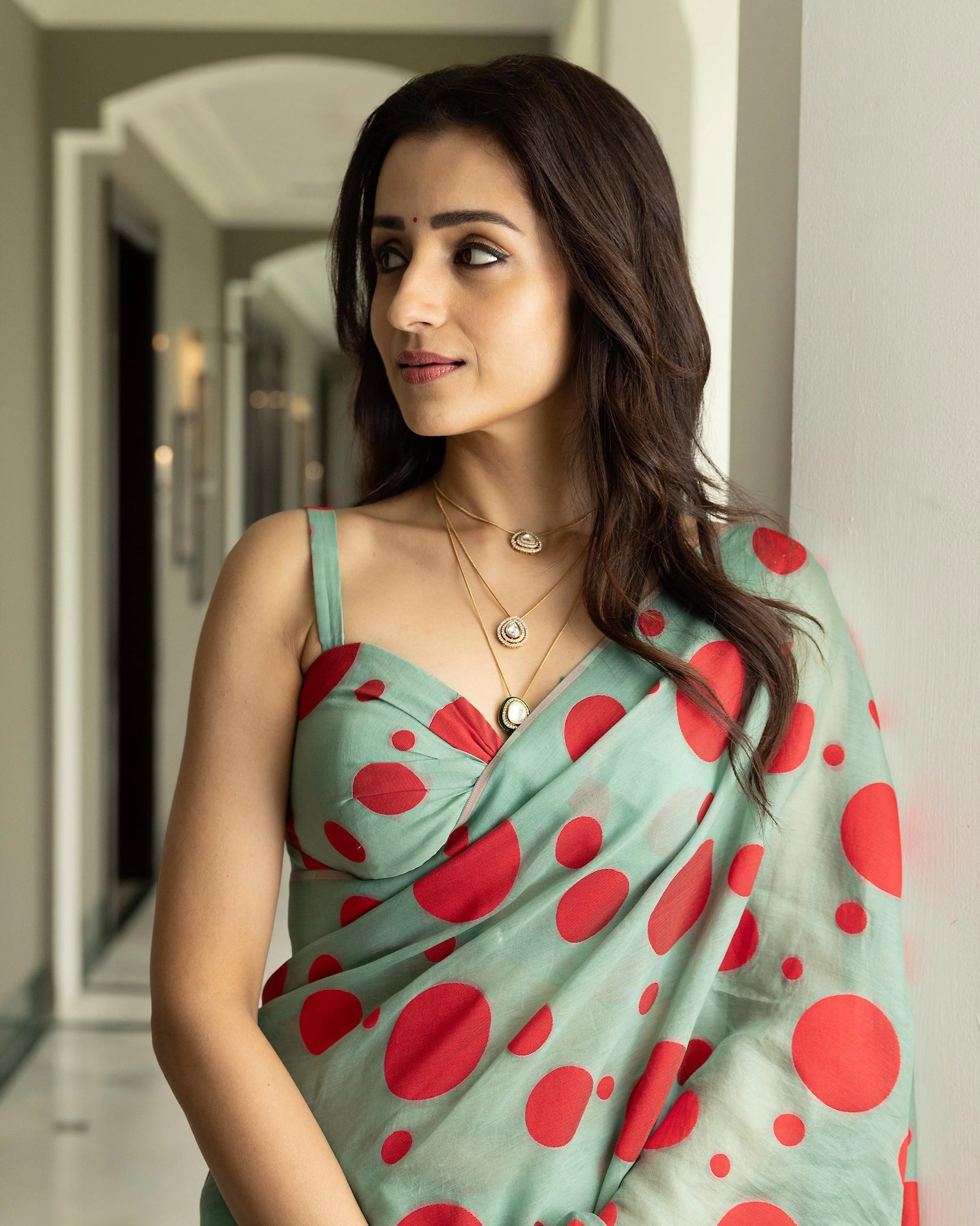 Indian woman in a green and red printed saree styled with layered necklaces and subtle makeup
