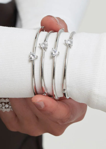 Elegant styling shot of a wrist adorned with multiple slim bangles featuring small diamond details, paired with layered rings.
