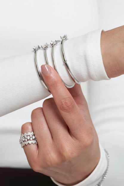 Fine jewelry composition showcasing polished metal bangles with subtle diamond accents, highlighted by a hand gesture.
