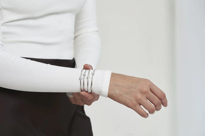 Minimalist close-up of stacked bangles on a white sleeve, complemented by sparkling multi-band diamond rings.
