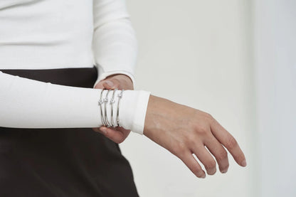 Contemporary jewelry look featuring smooth bangles with delicate stone settings, styled with a statement ring in a clean setting.
