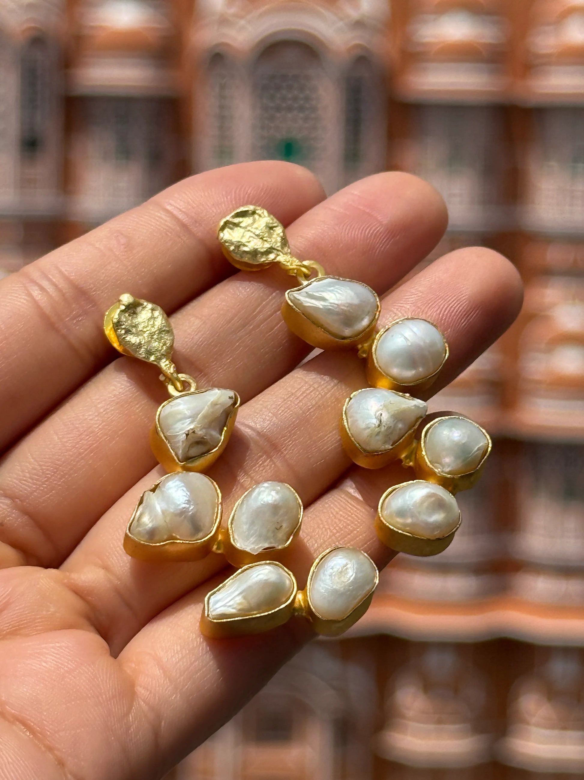 Hand holding designer pearl drop earrings with detailed palace facade in soft focus
