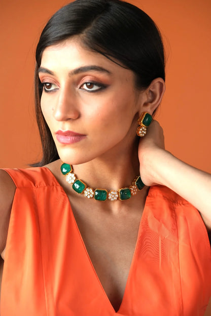 Elegant beauty detail highlighting a bold green stone stud earring accented with small pearls and textured gold.
