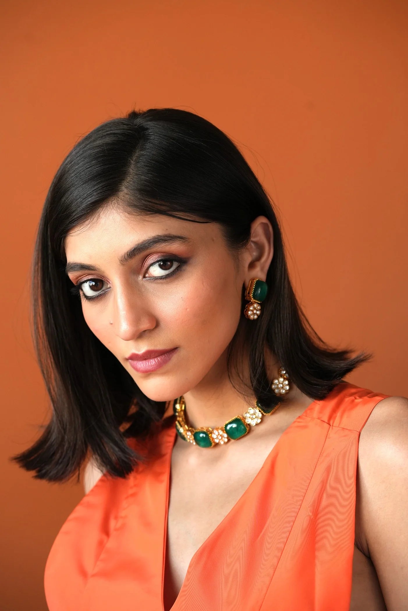 Fine jewelry close-up featuring a rectangular green gemstone earring with ornate gold work and delicate pearl drops.
