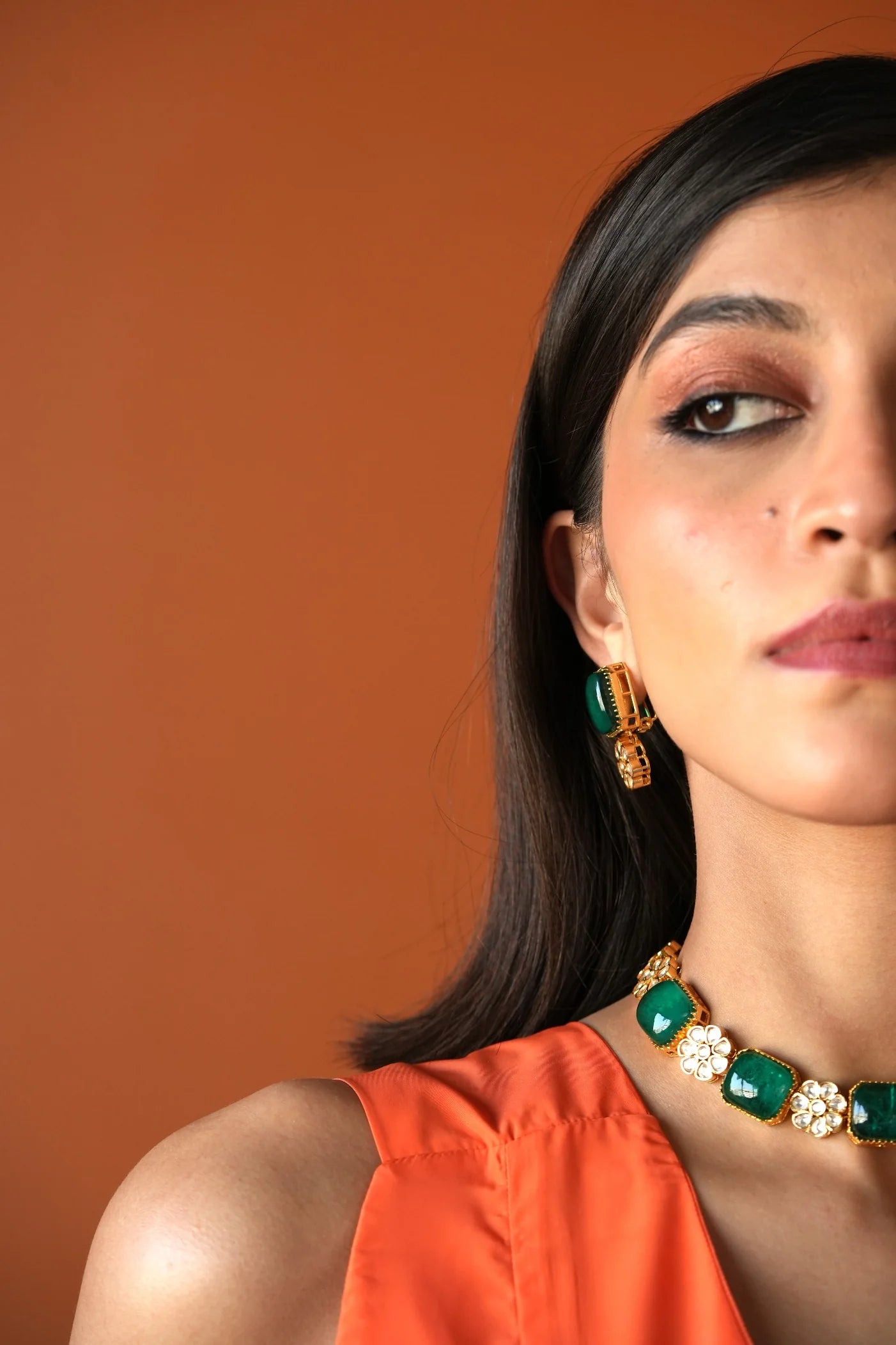 Luxury styling shot of a woman wearing a statement green and gold earring with intricate detailing and soft shimmer.
