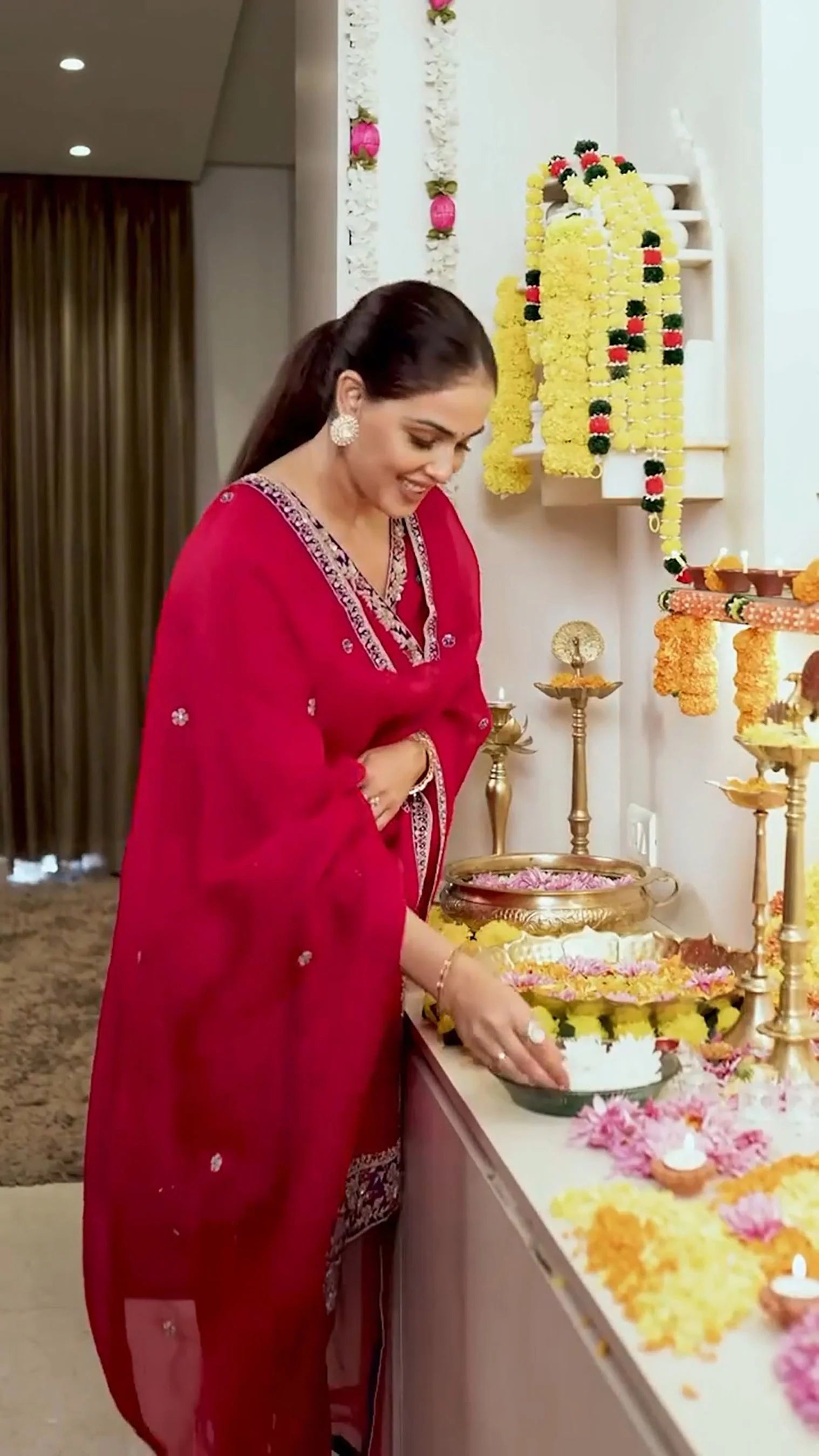 Indian woman in red kurta placing flowers on pooja thali with marigold garlands
