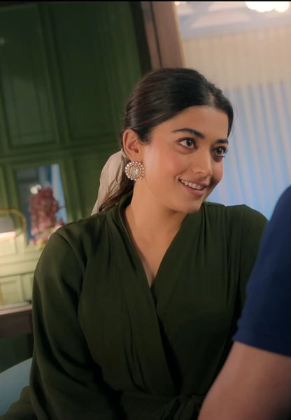 Woman smiling in red traditional attire arranging flowers near brass diya and garlands
