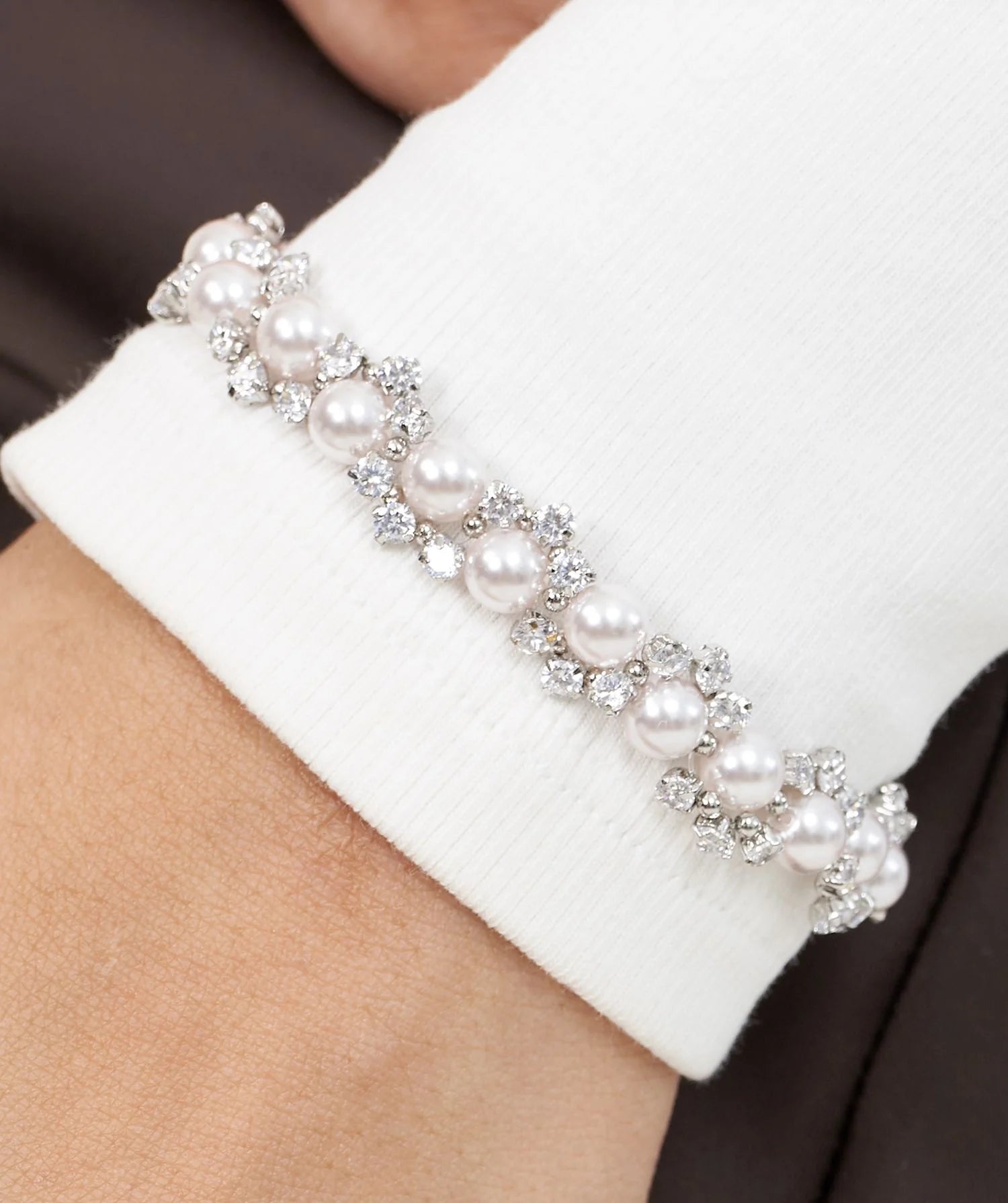 Elegant hand adorned with a dainty bracelet featuring alternating pearls and diamonds, set against a minimalist outfit.
