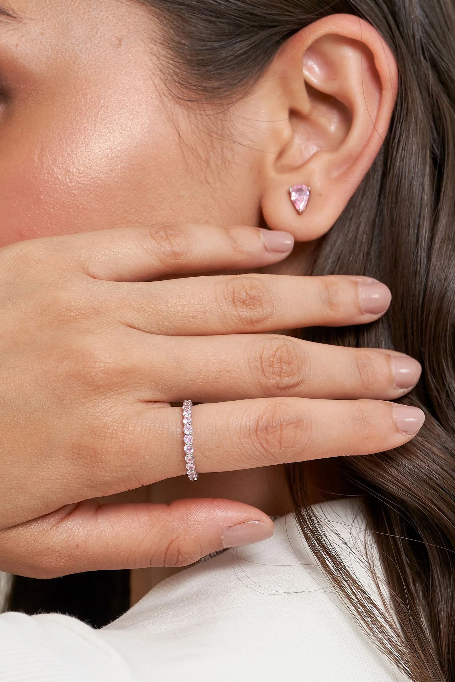 Elegant portrait of a woman partially covering her face, highlighting a slim diamond ring and a small colored gemstone earring.
