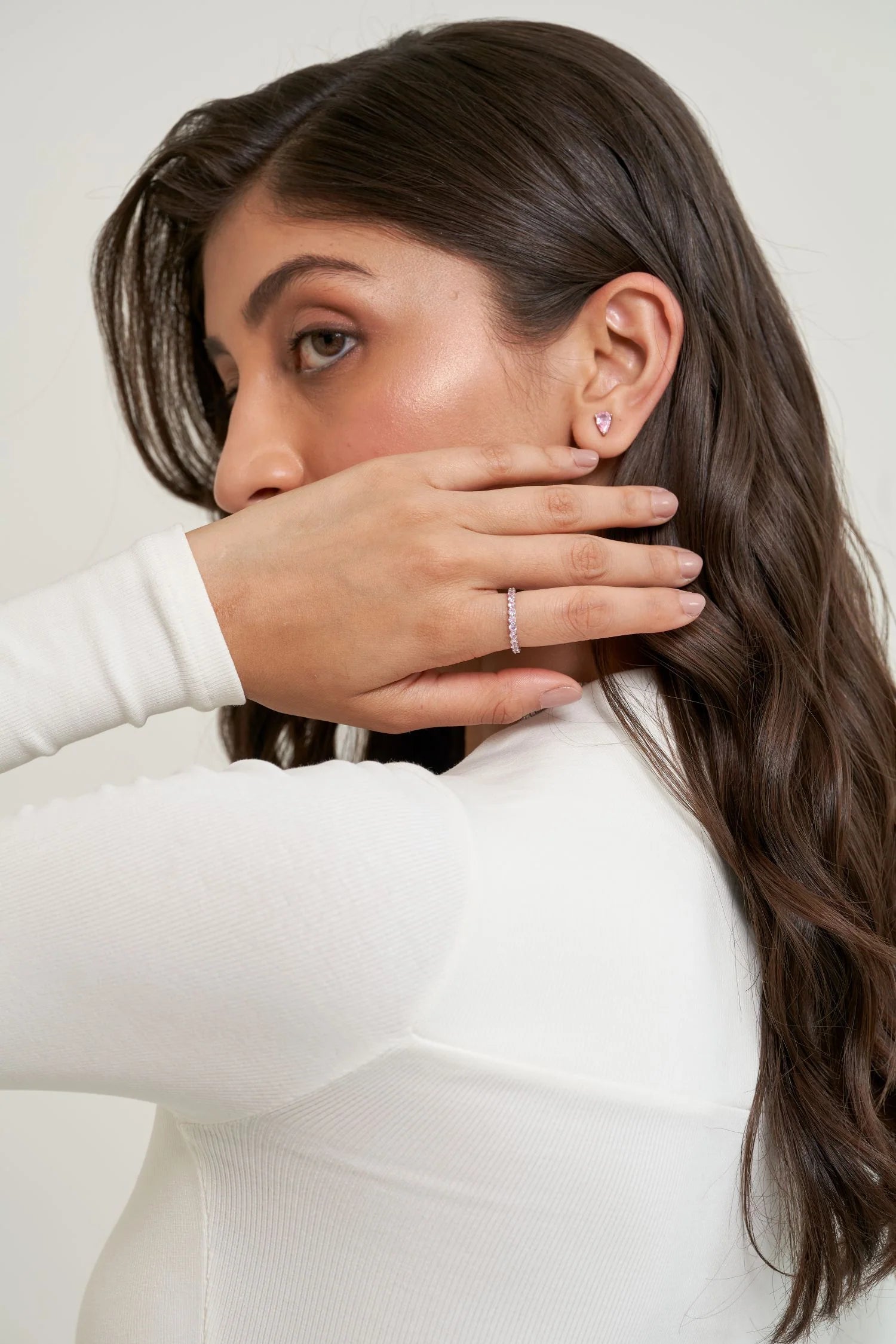 Minimal beauty shot featuring a hand with a fine diamond band placed over the face, paired with a dainty stud earring.
