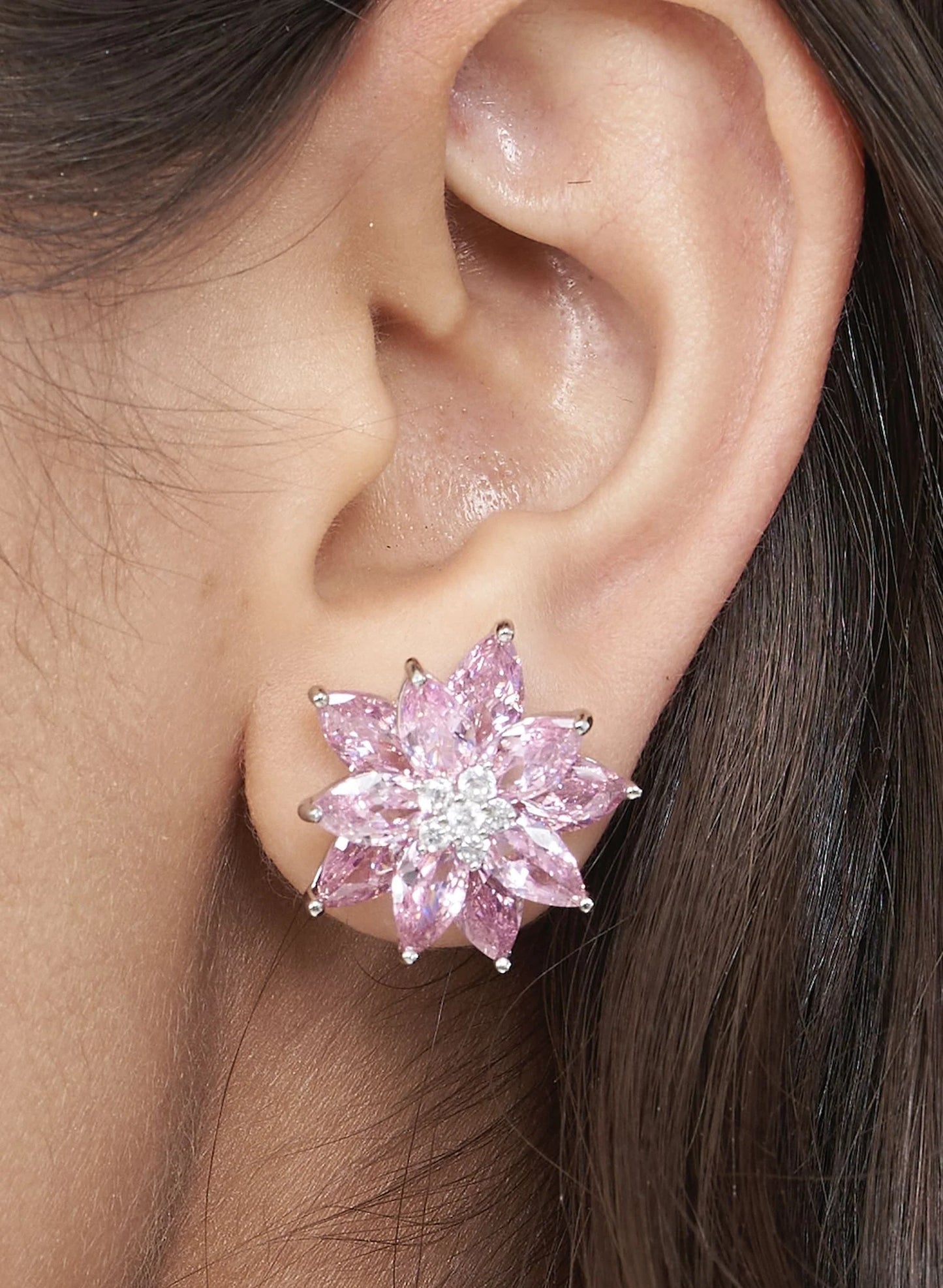 Fine jewelry close-up featuring a pink crystal stud earring arranged in a bold starburst pattern against soft skin tones.

