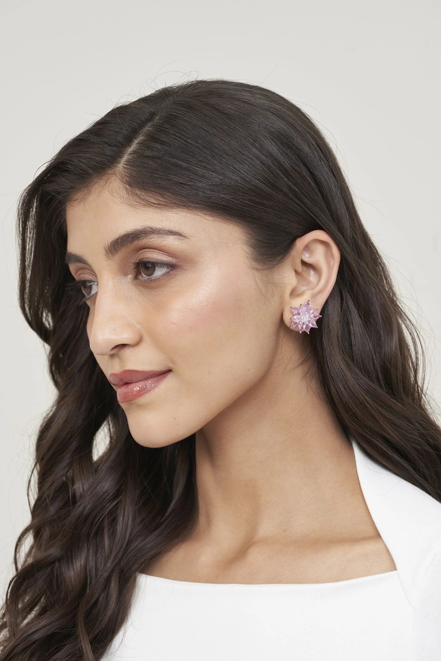 Close-up portrait of a woman wearing a pink starburst gemstone stud earring with a radiant multi-stone cluster design.
