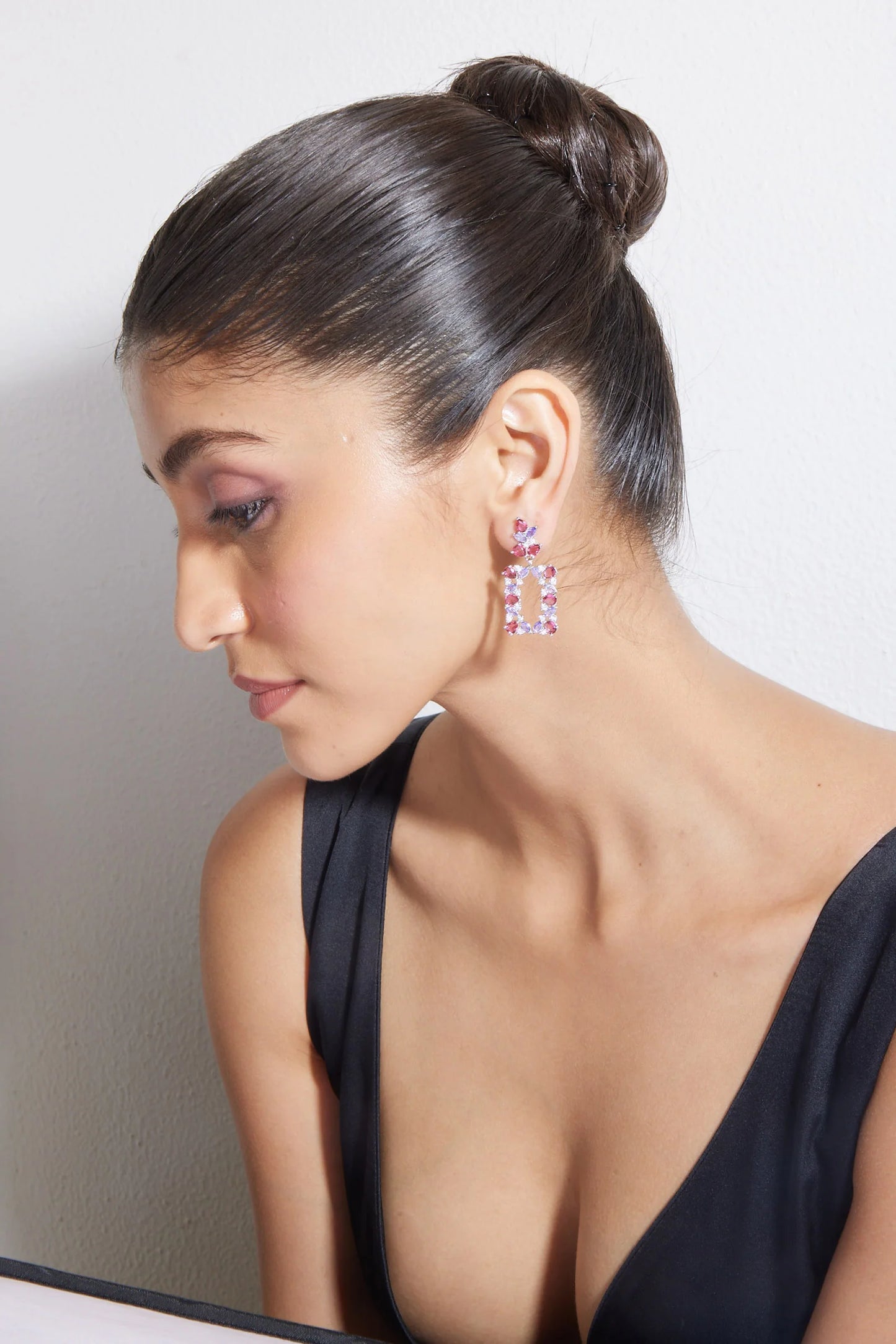 Fashion model showcasing pink gemstone statement earrings with dewy makeup and clean background
