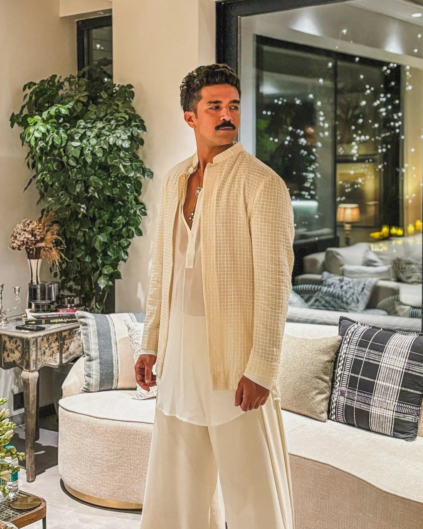 Elegant home setting featuring a man in light-colored outfit sitting casually on a plush sofa
