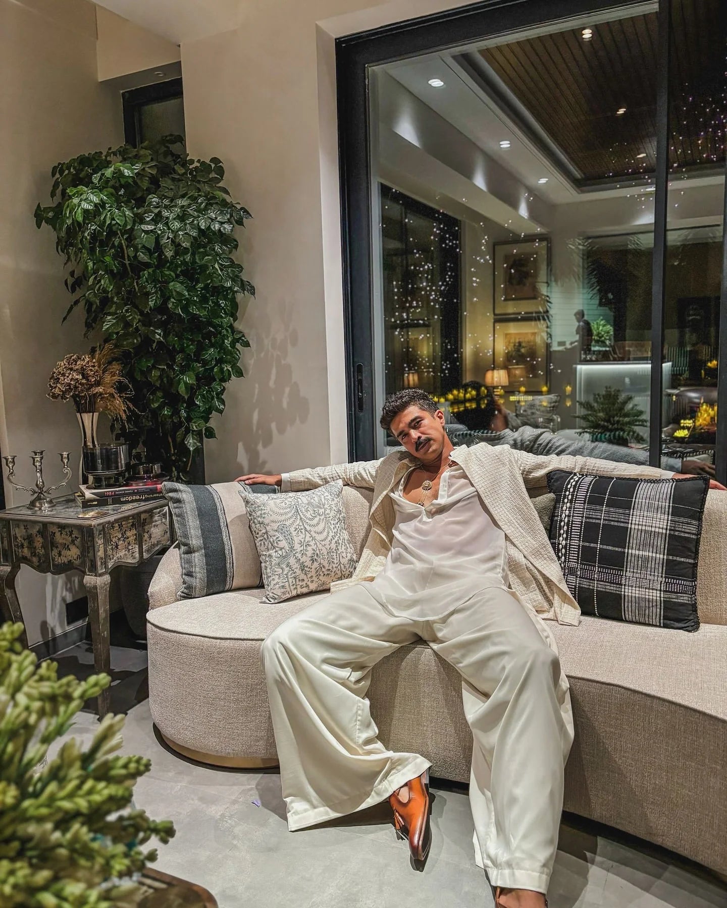 Nighttime indoor portrait of a man seated in a stylish living room with plants and glowing decor accents

