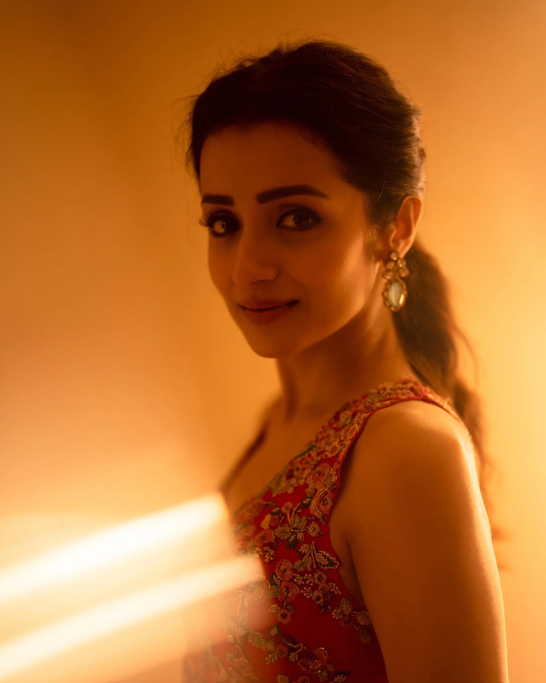 Close-up of a woman with soft glam makeup and ornate earrings in a red ethnic outfit with golden tones
