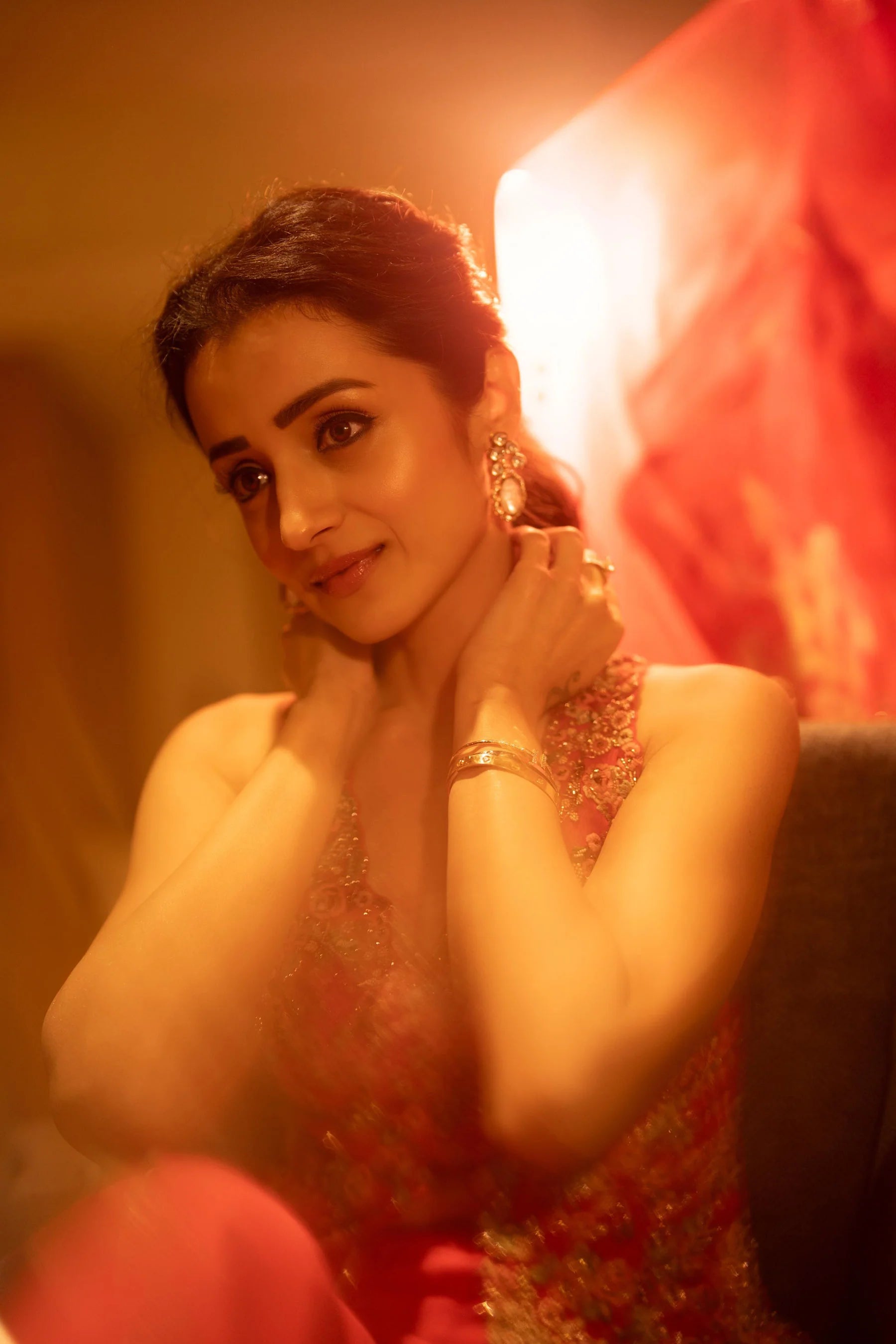 Fashion portrait of a woman in a red embroidered dress with statement earrings in warm ambient lighting
