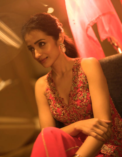 Woman wearing a traditional red outfit with intricate embroidery and elegant earrings in golden light
