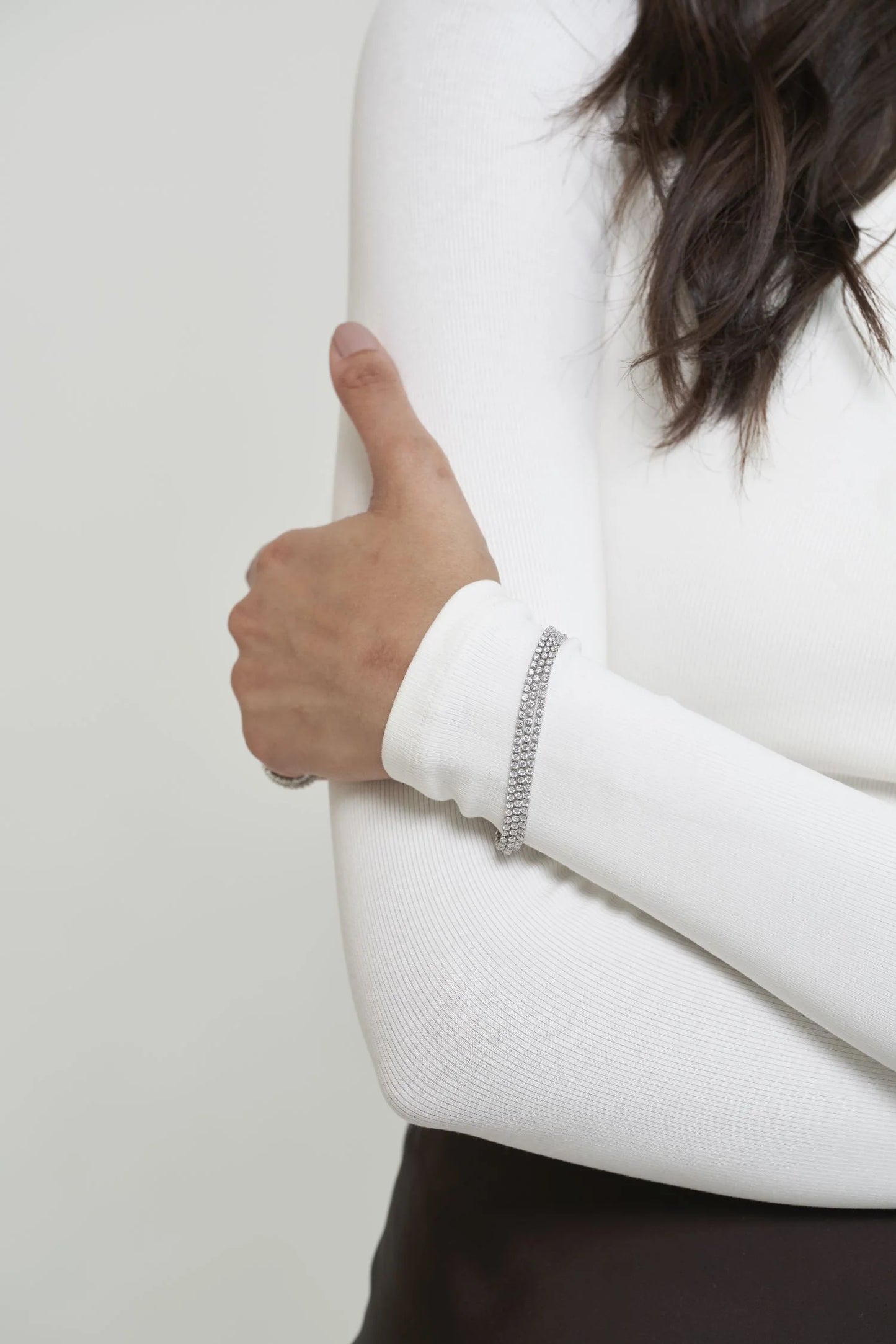 Refined white gold bracelet with multiple diamond lines and a modern interlocking design, styled with a sleek long-sleeve top.
