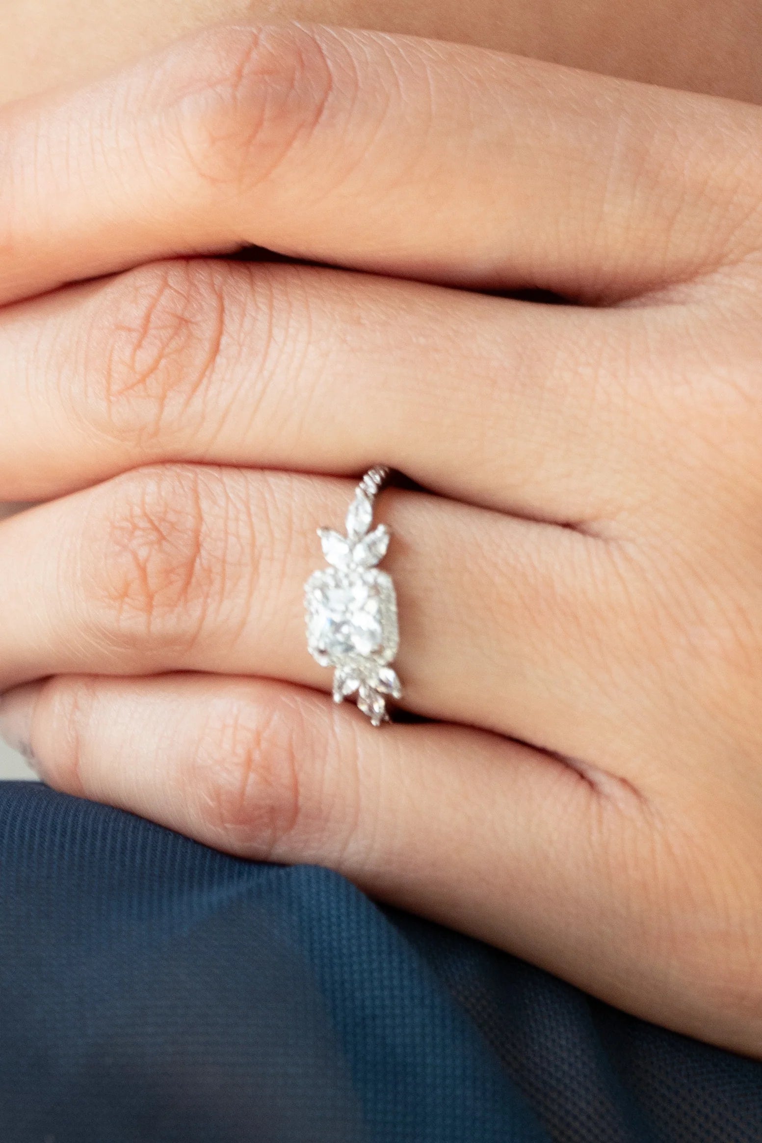 Close-up of a hand wearing a diamond ring with a central cushion-cut stone accented by marquise side details in a delicate white gold setting.
