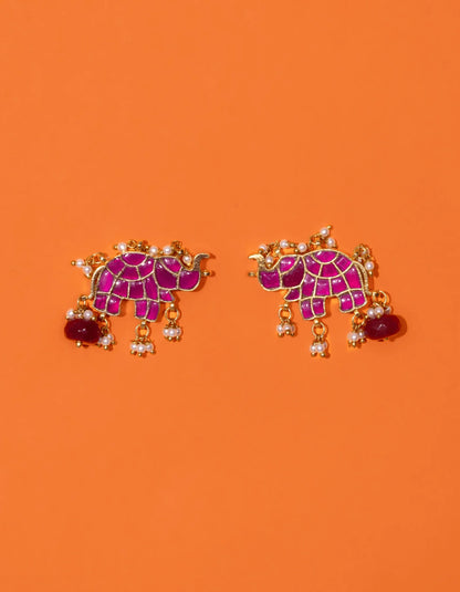 Elegant side detail of a woman wearing a colorful gemstone earring with layered pearl embellishments, set against a creative, paint-accented composition.
