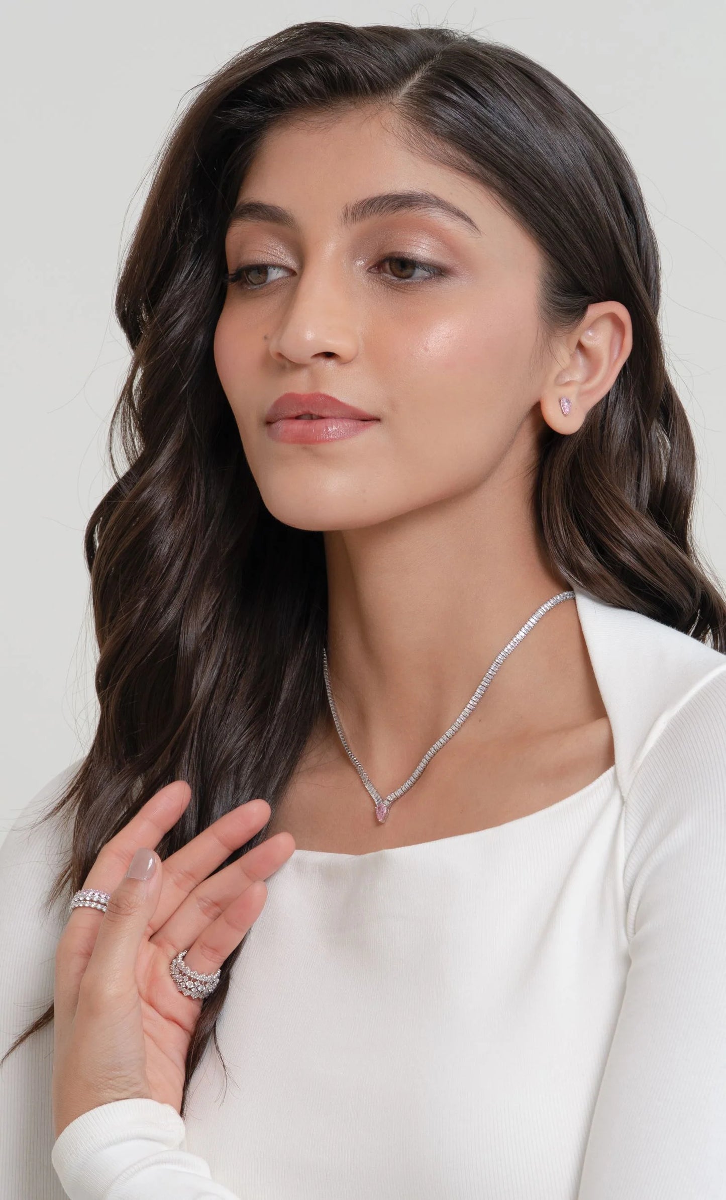 Elegant beauty shot of a woman adorned with fine diamond jewelry including a pendant necklace, rings, bracelet, and subtle stud earrings.
