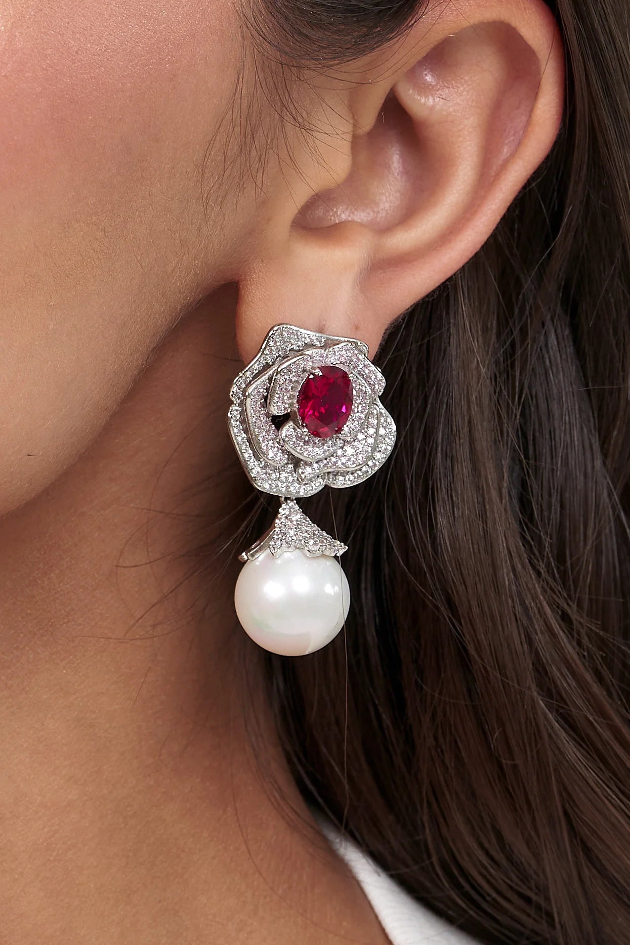 Elegant side profile highlighting a flower-inspired earring with a ruby-toned gemstone center and a dangling pearl accent.
