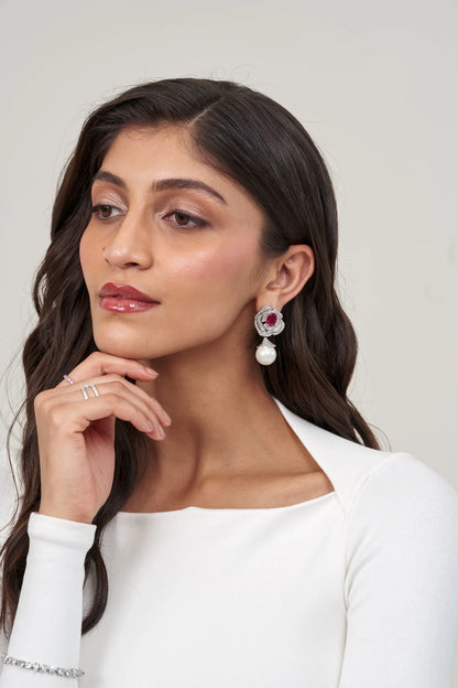 Detailed portrait of a woman wearing a statement floral earring combining a vibrant pink stone, sparkling halo, and pearl pendant.
