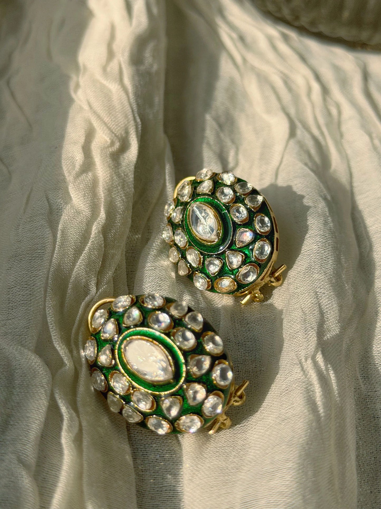Close-up of layered gold chains with emerald centerpiece on fabric-draped bust
