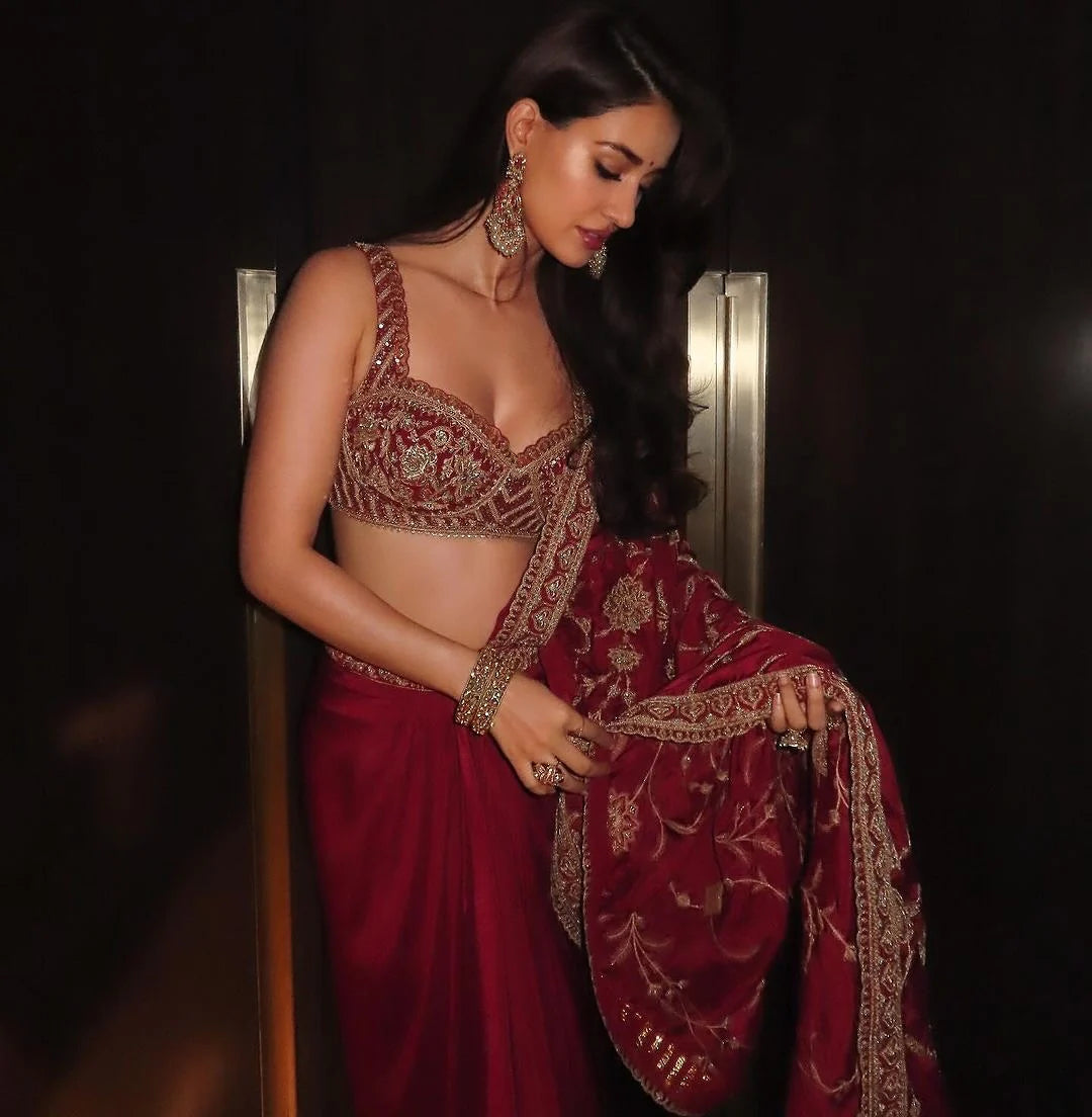 Elegant fashion shot showcasing a woman in a richly embellished red ensemble with ornate embroidery and bold statement earrings.
