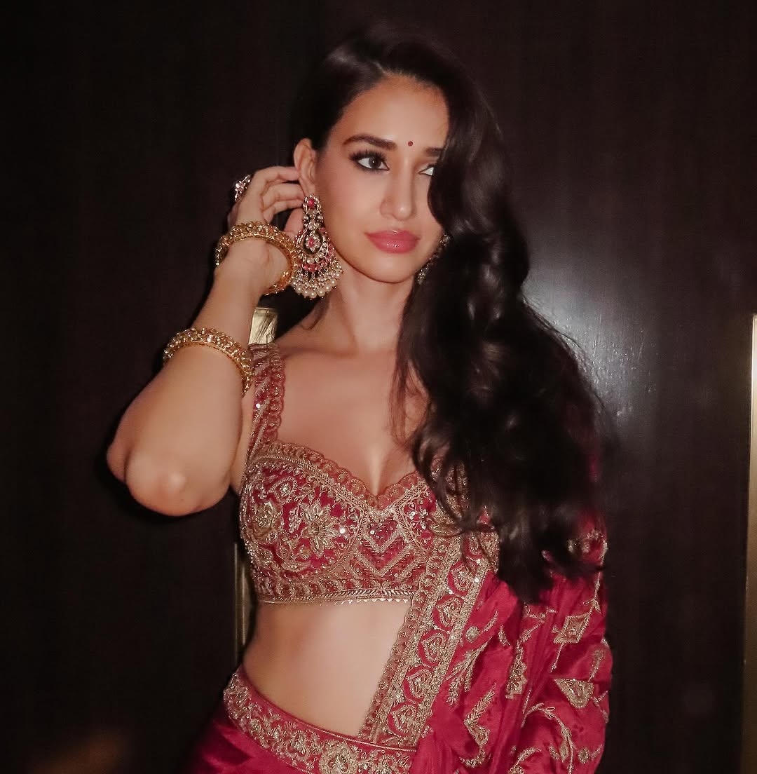 Fine fashion close-up featuring a woman in a red lehenga with ornate patterns, accessorized with a bracelet and statement earrings.
