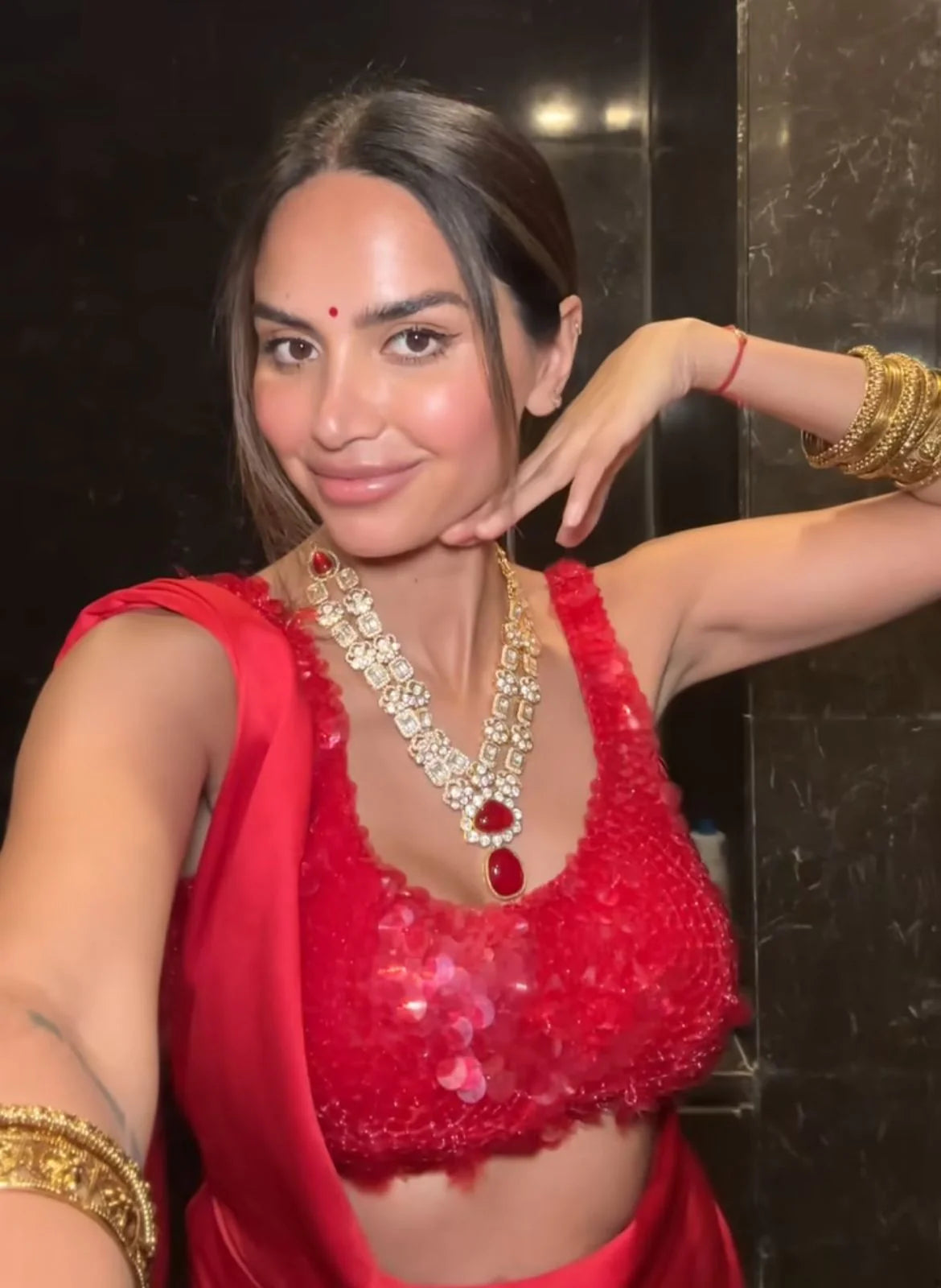 Social event portrait of two women in festive attire, one in a bright red ensemble and the other in a black saree with gold detailing.
