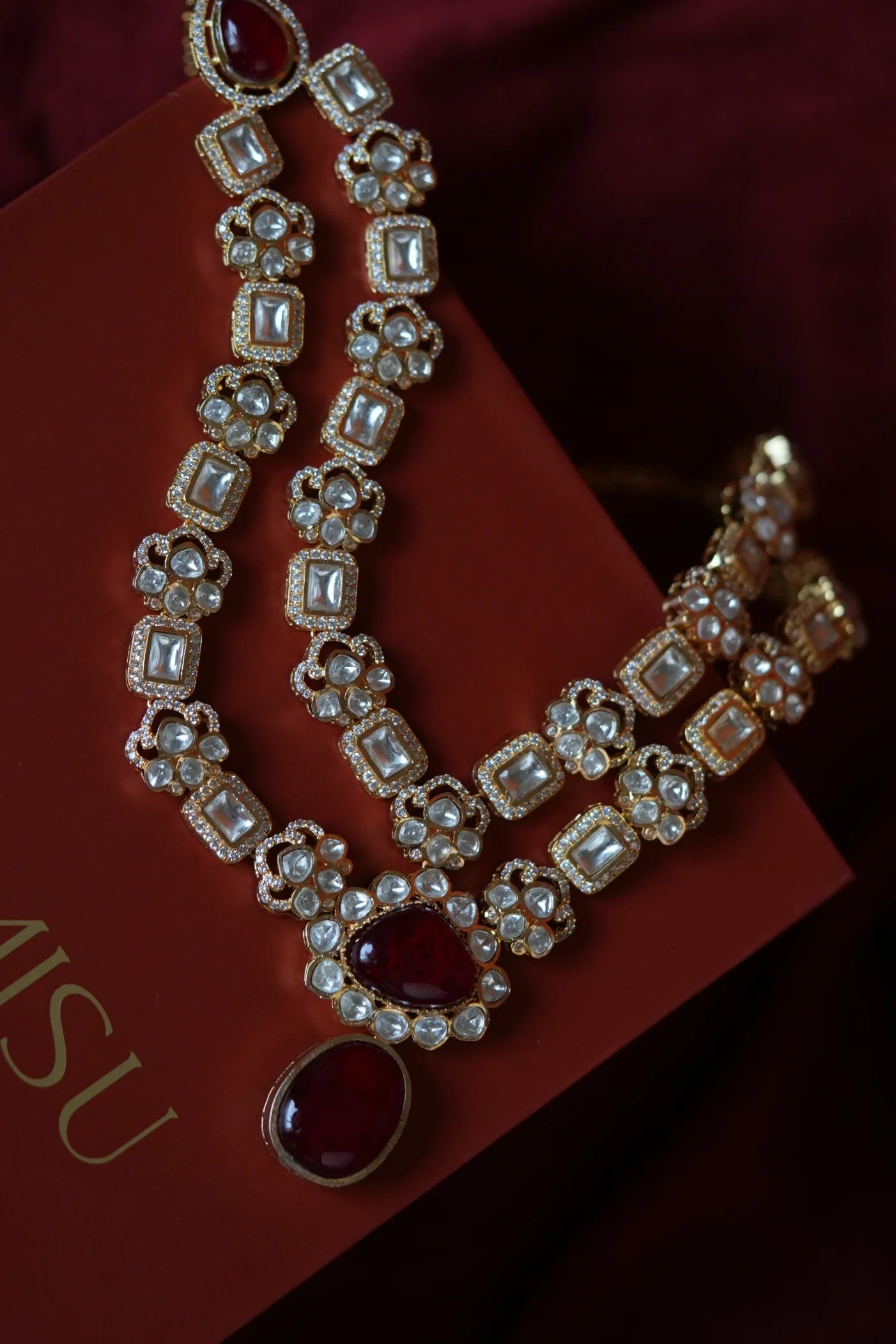 Elegant party scene featuring two women dressed in a red co-ord set and a black and gold traditional outfit, smiling at the camera.
