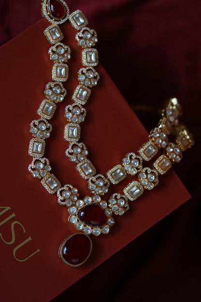 Elegant party scene featuring two women dressed in a red co-ord set and a black and gold traditional outfit, smiling at the camera.
