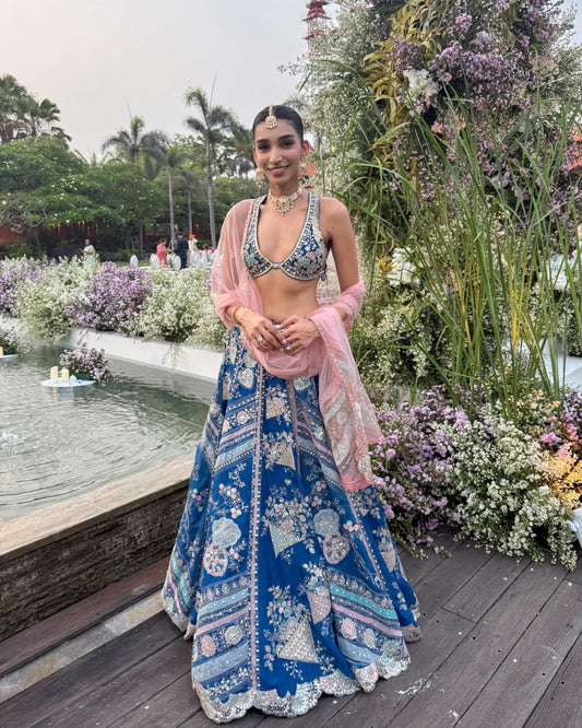 Festive fashion shot featuring a woman in a blue and pink traditional outfit with intricate embroidery, styled with a choker and maang tikka.
