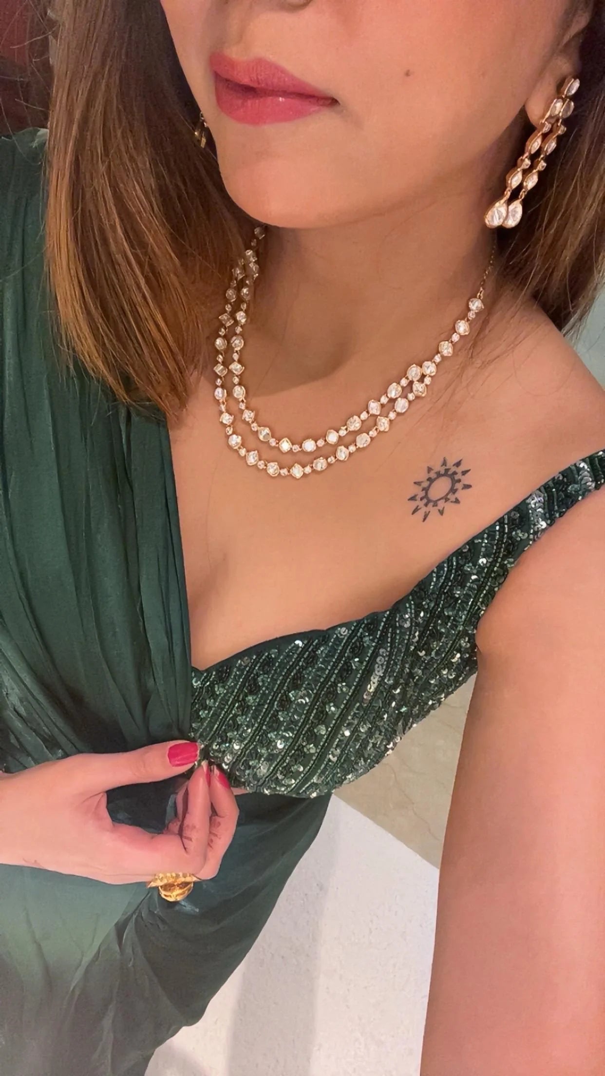 Close-up side profile of a woman wearing layered diamond necklaces and long drop earrings with teardrop stones in a warm-toned setting.
